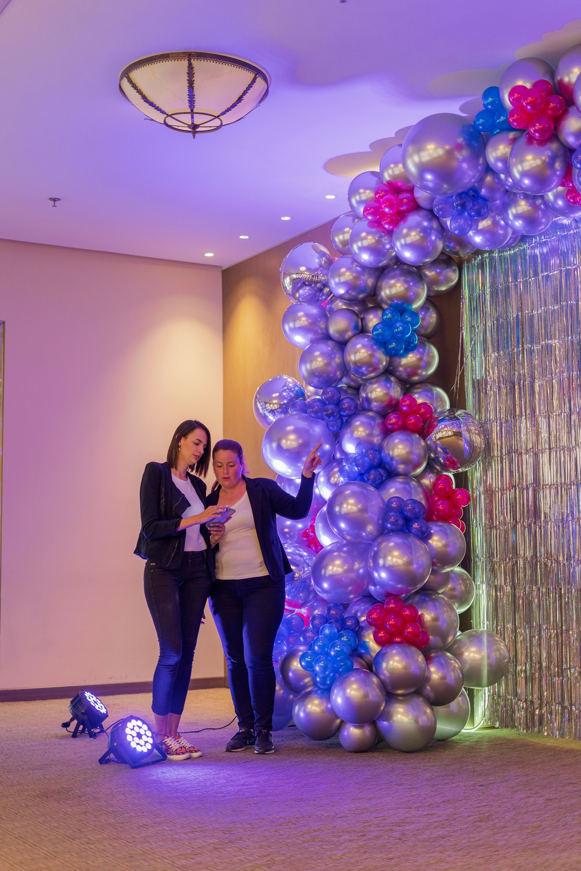 two latin women party decorators are close to one of their balloon creations analyzing small details